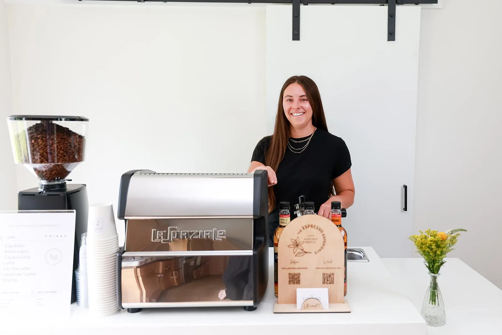 Smiling barista standing behind the mobile espresso cart with grinder and syrups