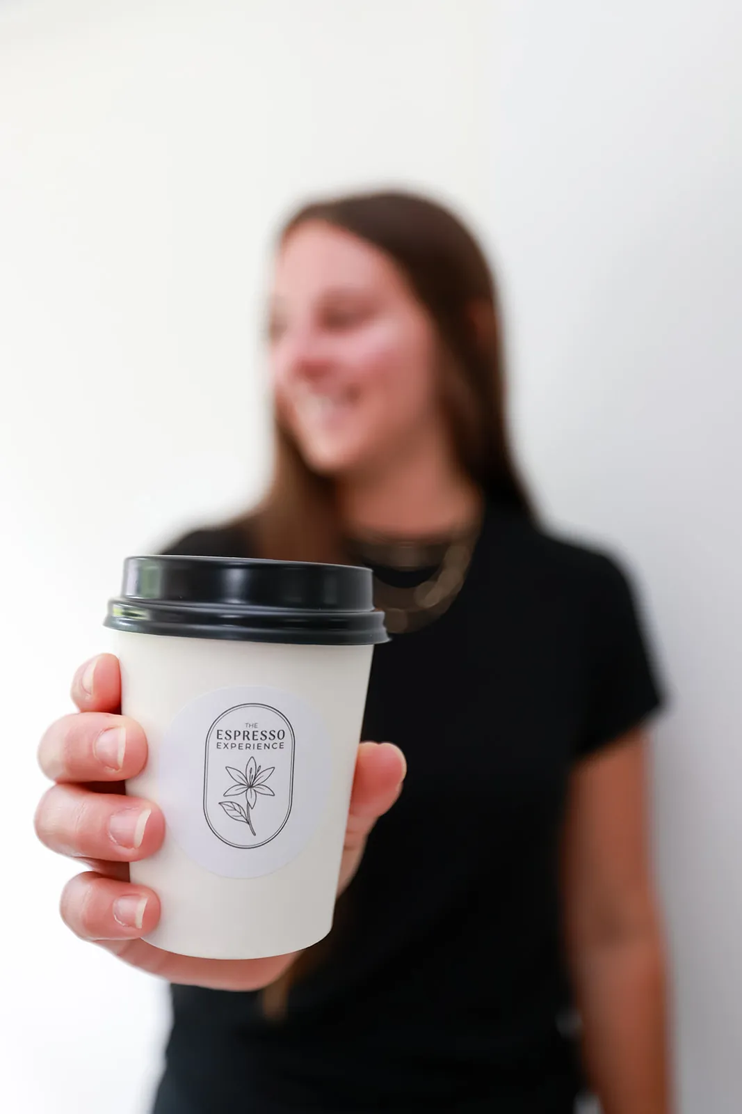 Branded hot coffee cup with a black lid held toward the camera
