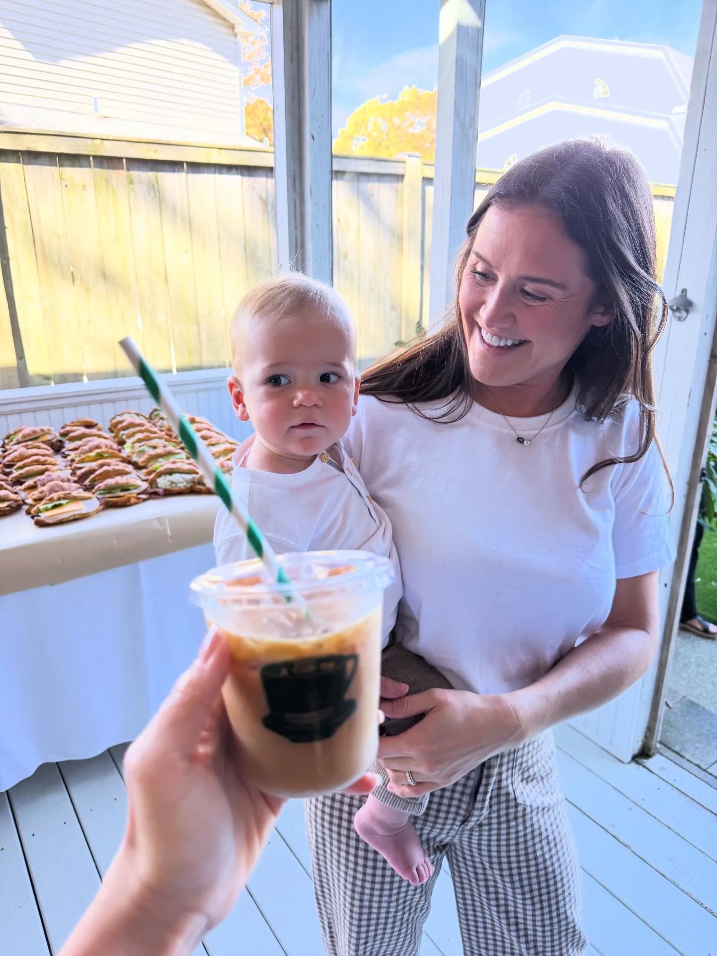 Guest holding a baby and an iced coffee at a backyard party