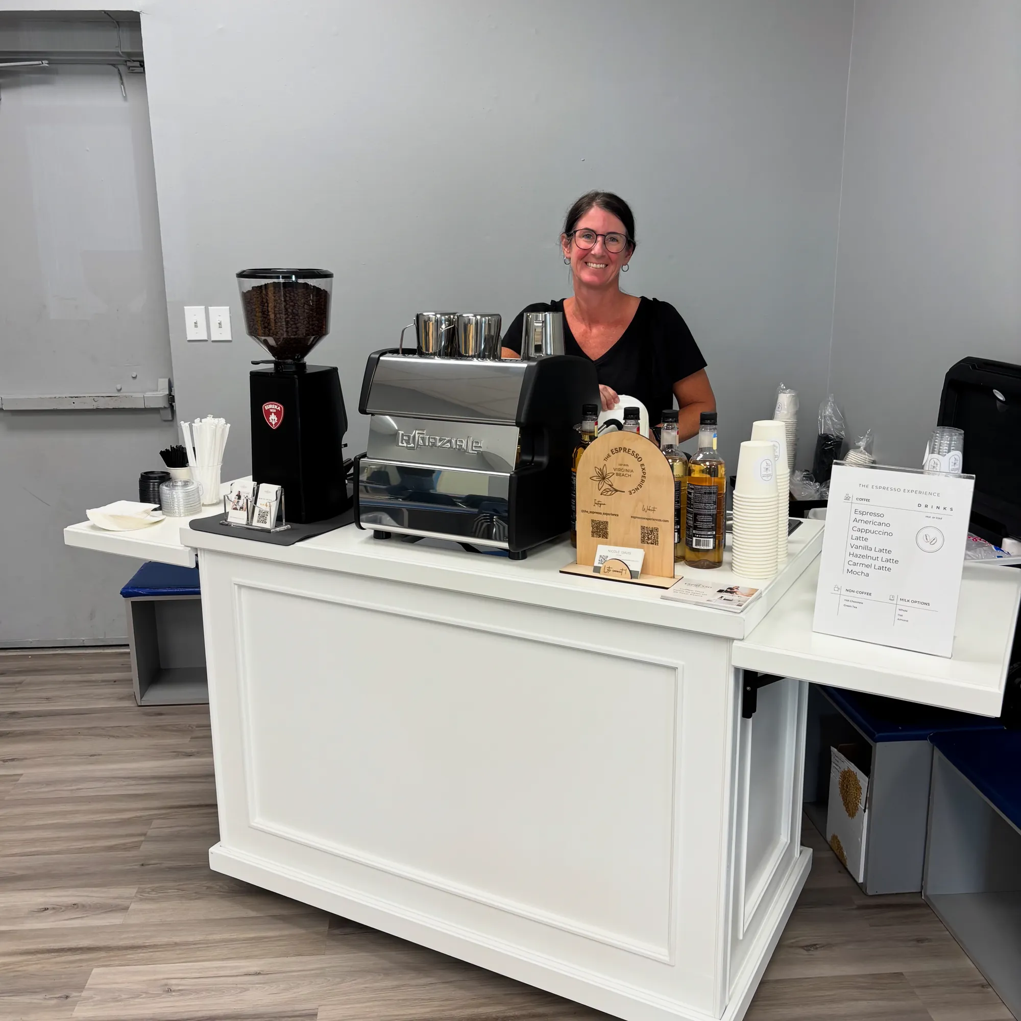 Barista serving from the white espresso cart at an indoor office event